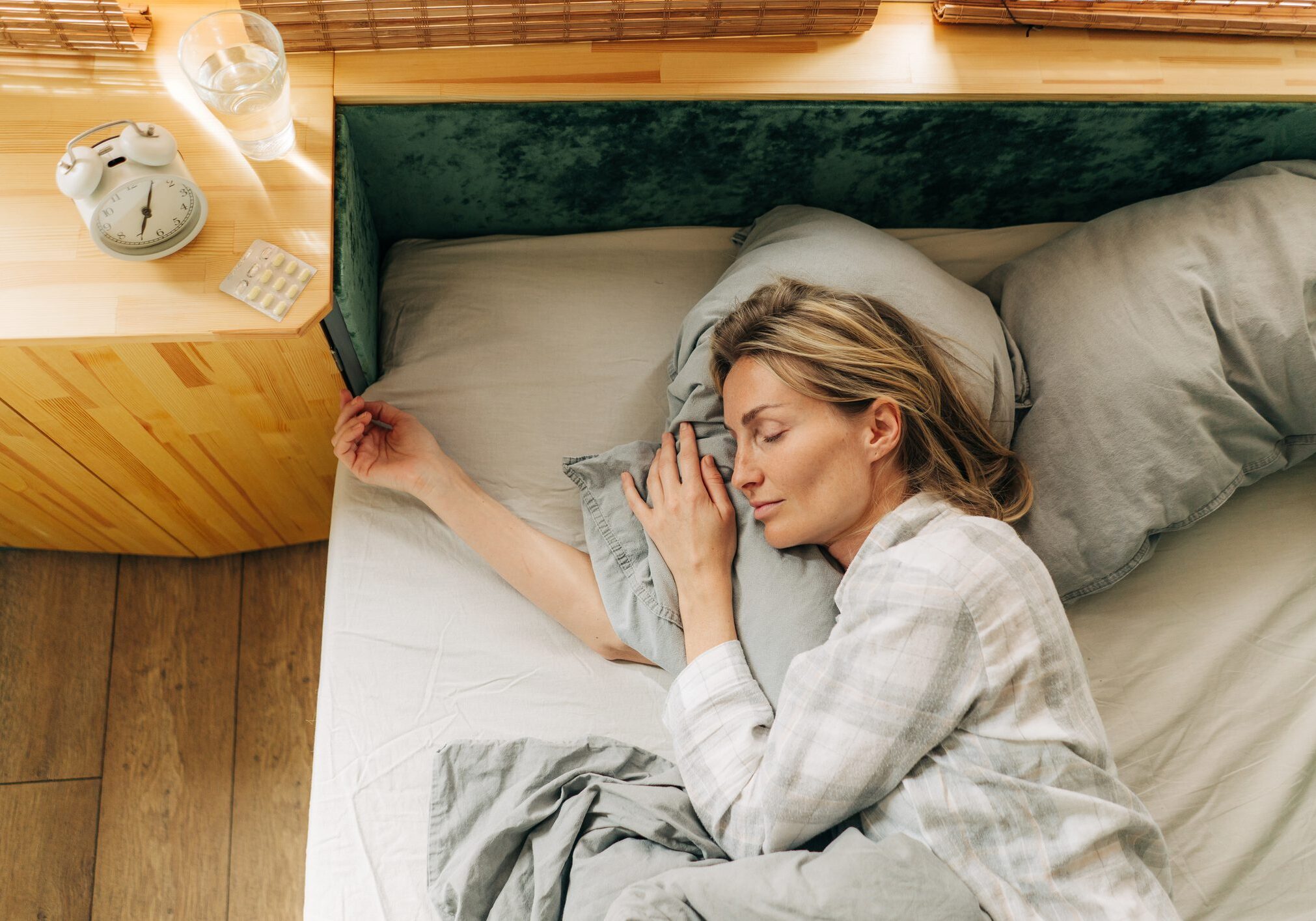 A woman sleeps blissfully in her bed, on the bedside table an alarm clock and pills for insomnia.